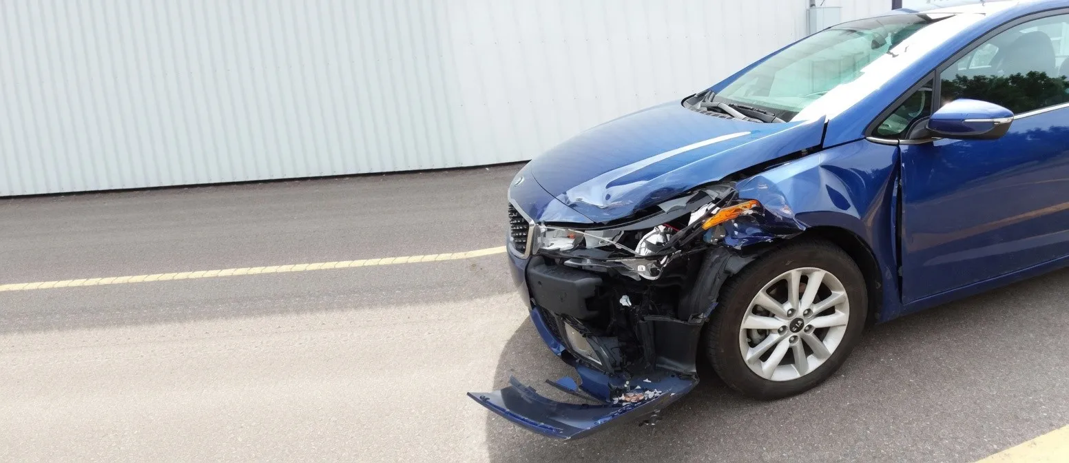 Blue Kia Forte with front-end collision damage at Spanky's Collision Repair in Hudsonville, MI