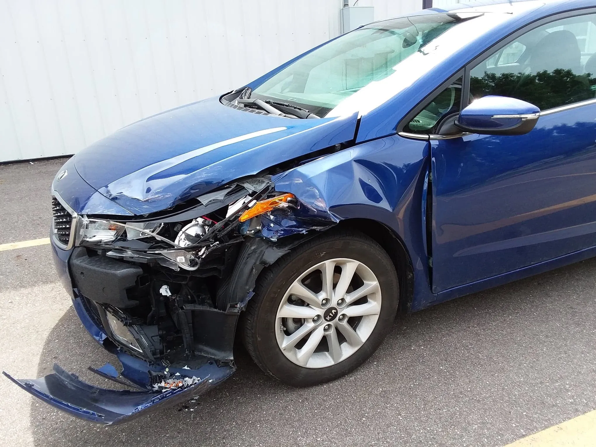 Blue Kia Forte with front-end collision damage in the shop at Spanky's